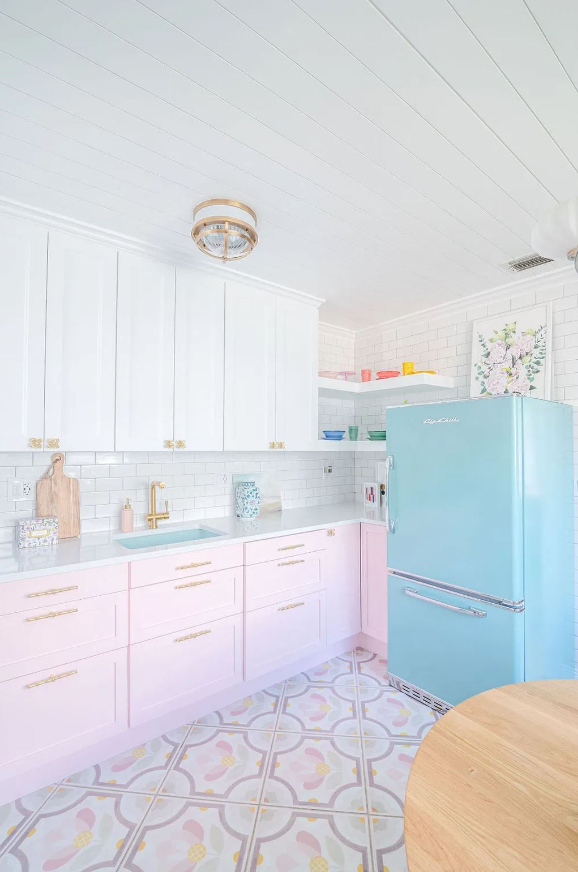 Pink painted cabinets, a colorful floor, bright blue fridge, and white cabinets and subway tile in a custom kitchen.