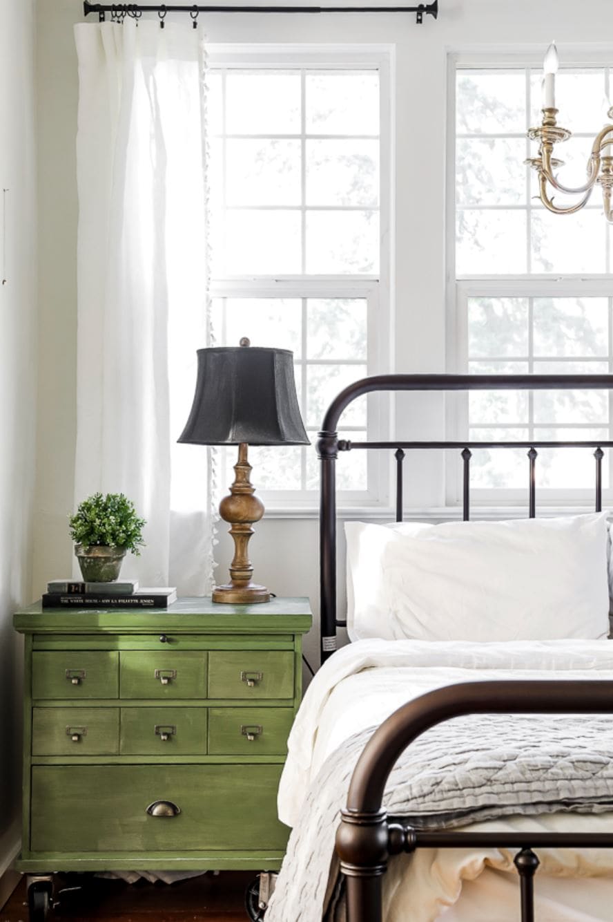 IKEA curtains hanging in a bedroom with a green card catalog nightstand and an iron bed.