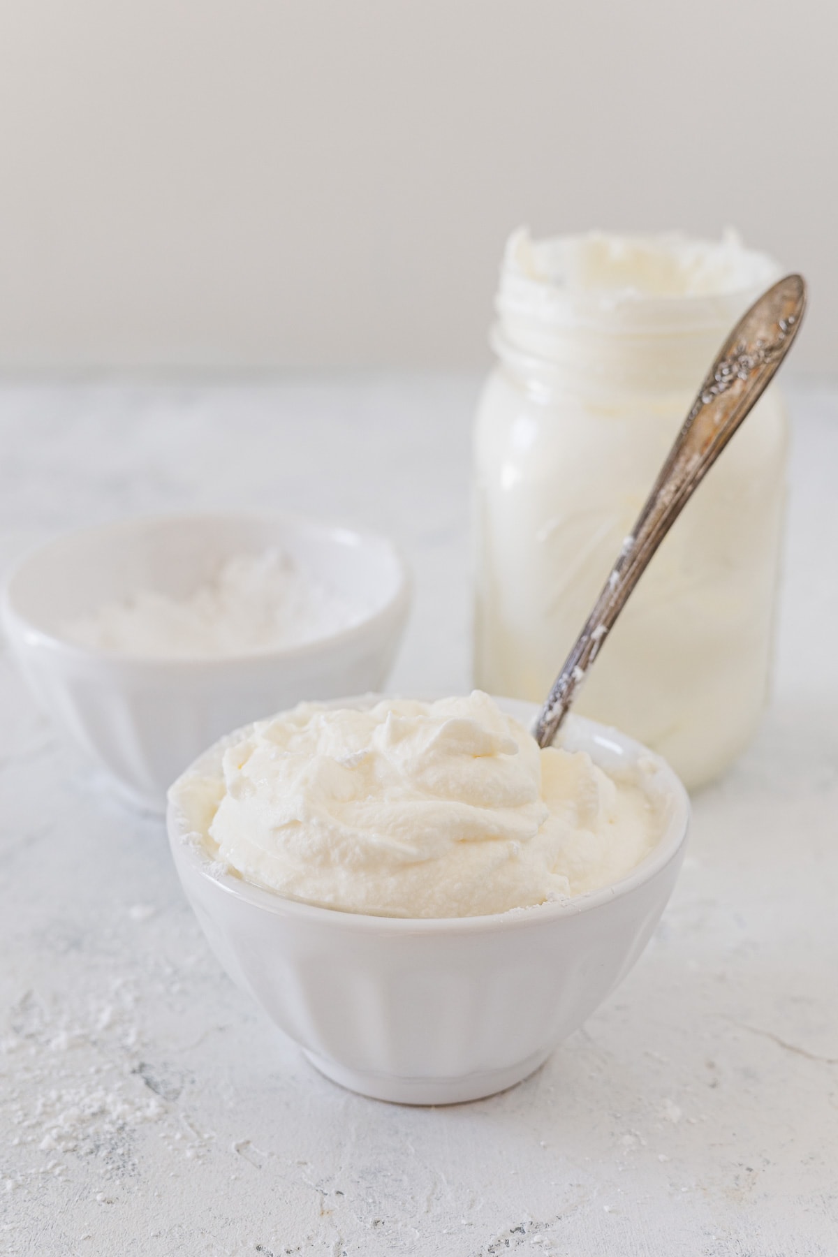 A white bowl filled with homemade whipped cream and sugar and a mason jar in the background.