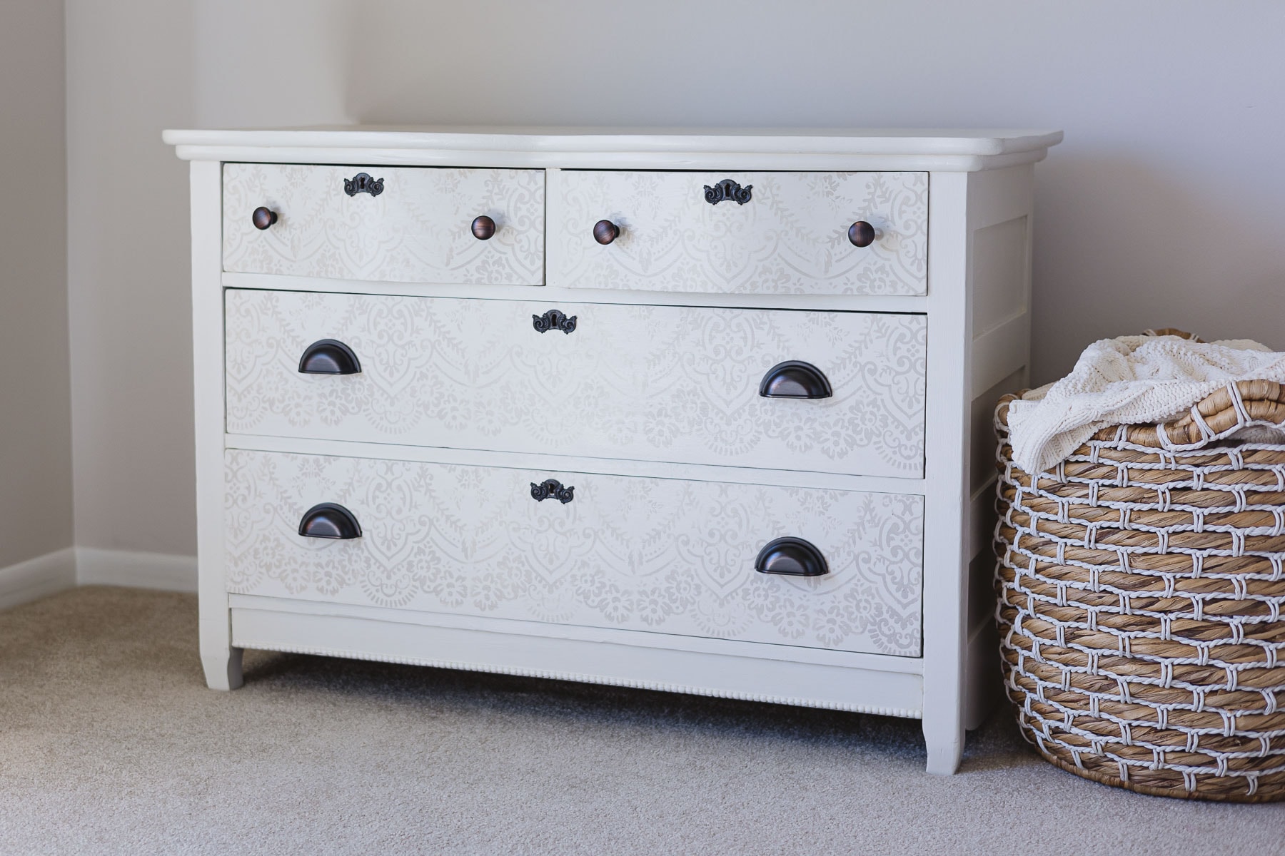 A vintage dresser painted white and stenciled with a very light brown with oil rubbed bronze hardware.