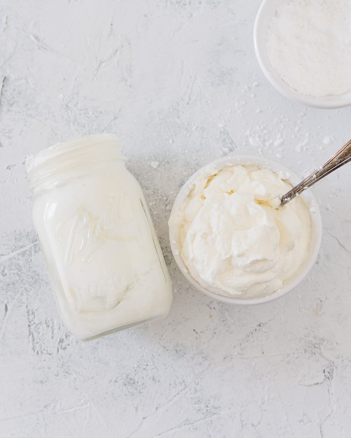 A mason jar used for homemade whipped cream and a bowl full of whipped cream.