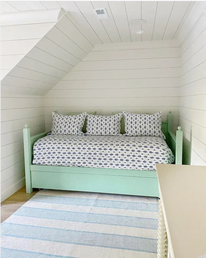 Attic bedroom with white shiplap walls and ceiling and a green trundle bed.