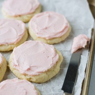 A parchment-lined cookie sheet filled with pink-frosted sugar cookies and a knife with frosting on it.