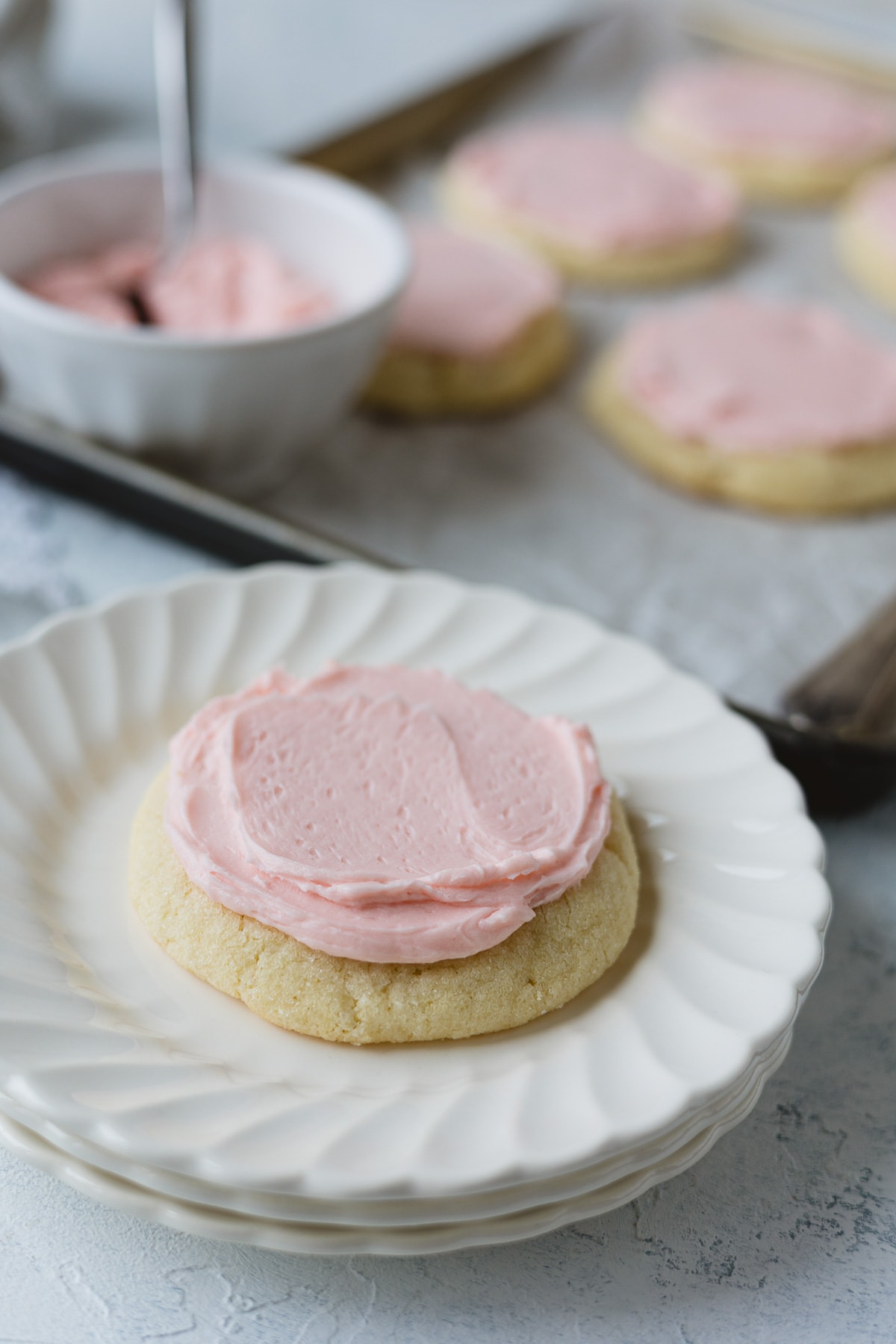 A pink frosted Crumbl copycat sugar cookie on a stack of small scalloped plates.