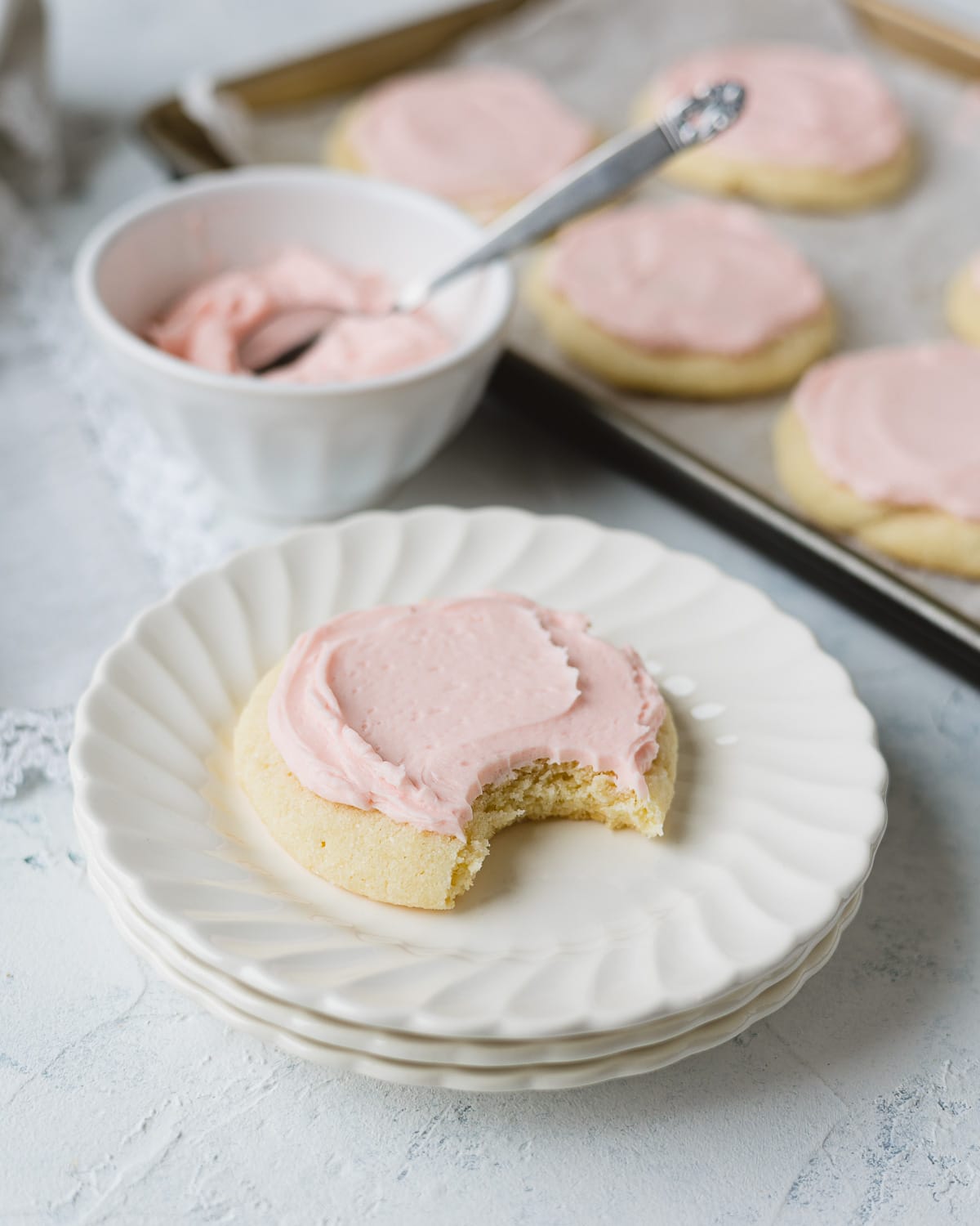 A Crumbl copycat Pink Sugar Cookie with a bite removed on a stack of small scalloped plates.