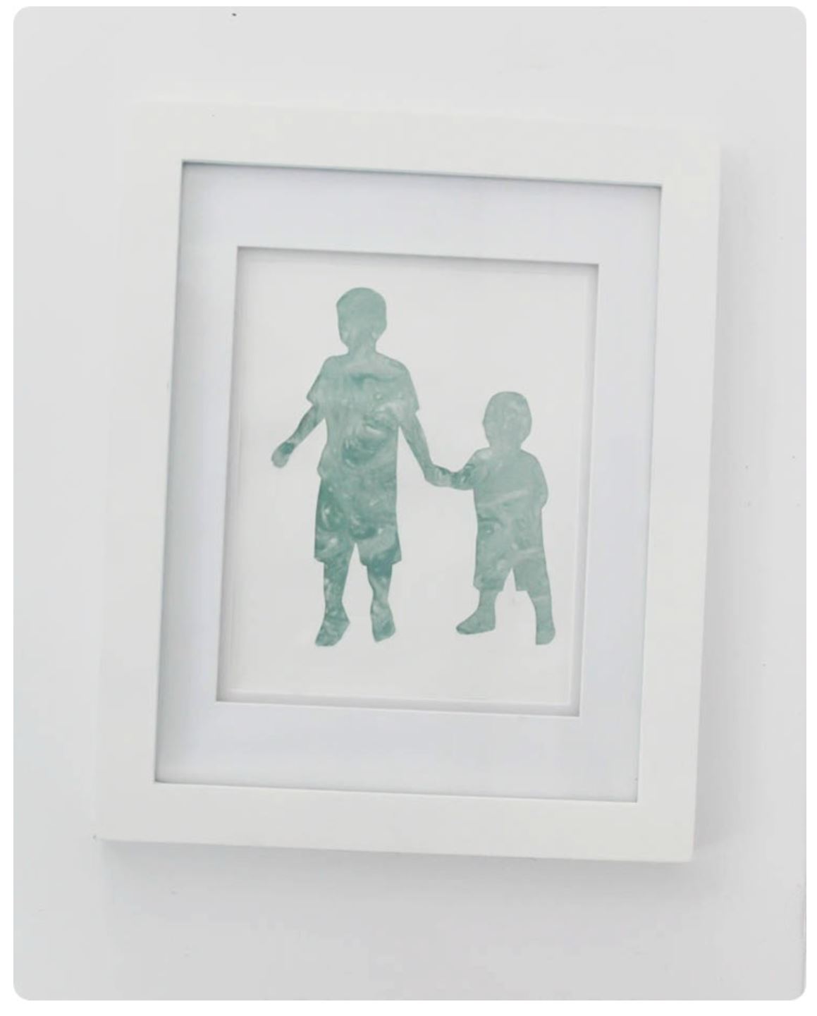 A framed silhouette print of two children holding hands.