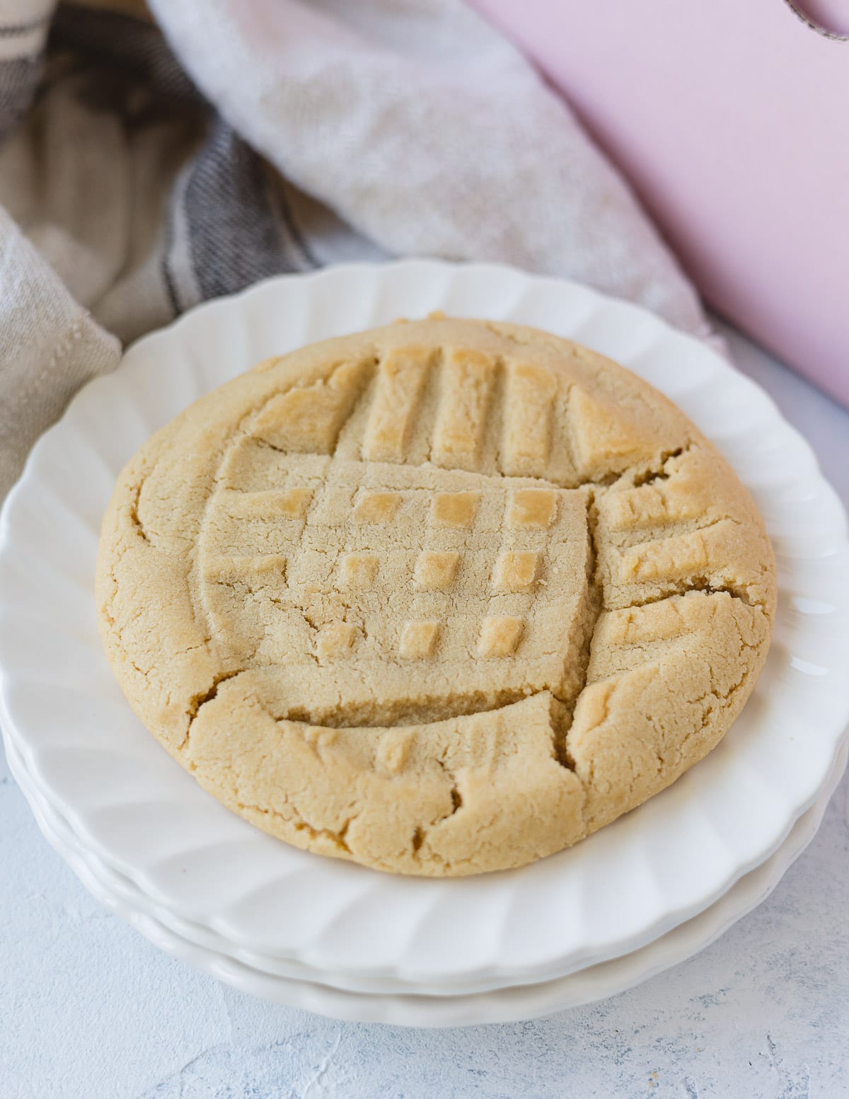 A large peanut butter cookie on a stack of three scalloped plates.