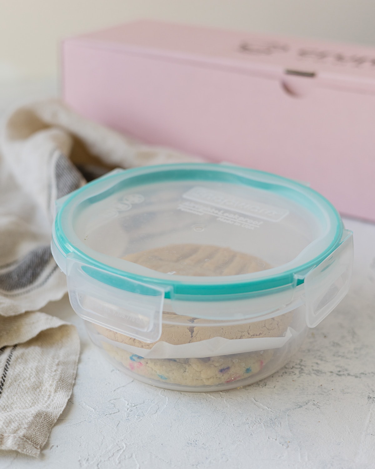 A closed plastic container with cookies inside separated by parchment paper.