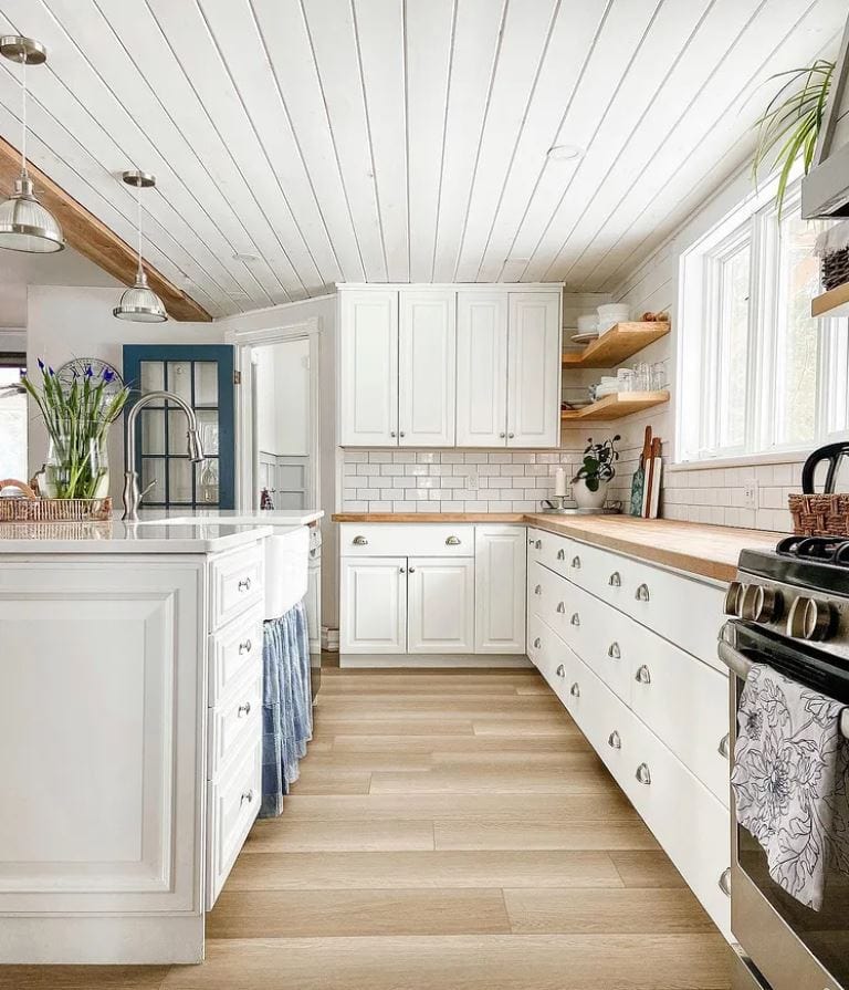 A white planked ceiling in a white kitchen with wood floors, countertops, and open shelving.