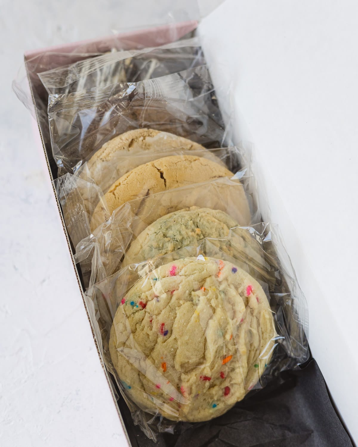 A row of individually packaged Crumbl Cookies in a tissue-lined shipping box.