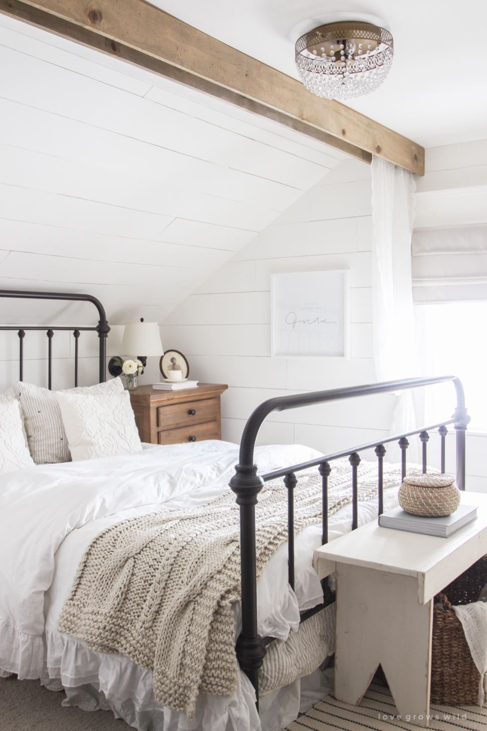 A farmhouse bedroom with iron bed frame, white bedding, and shiplap walls and ceiling.