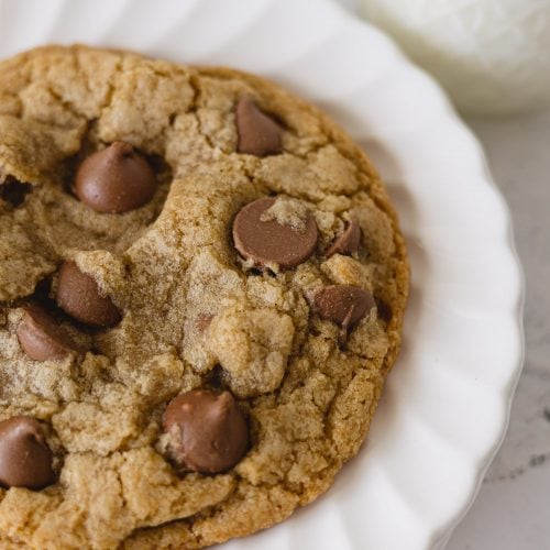 A closeup view of a chocolate chip cookie with jumbo milk chocolate chips on a stack of white scalloped plates.