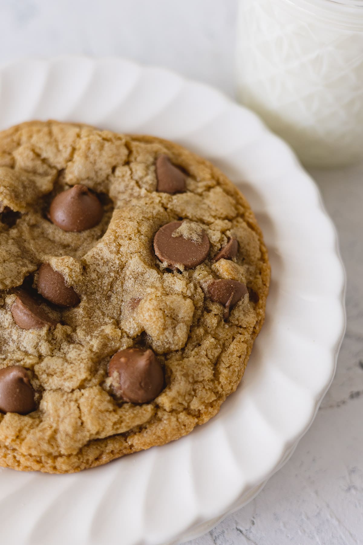 A closeup view of a chocolate chip cookie with jumbo milk chocolate chips on a stack of white scalloped plates.