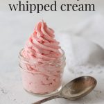 Pink whipped cream piped into a small mason jar with a vintage spoon nearby with the words, "Strawberry Whipped Cream".