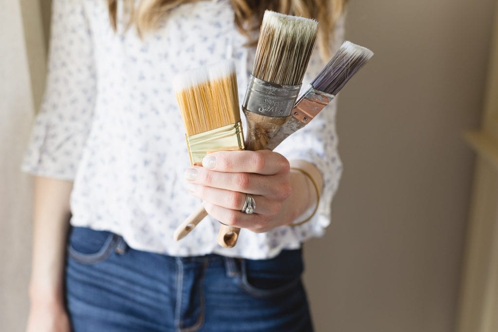 Woman holding three different paint brushes.