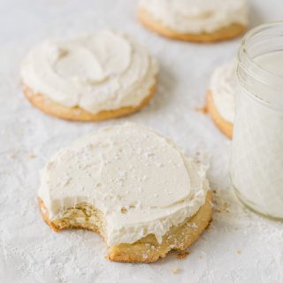 A vanilla frosted sugar cookie sprinkled with powdered sugar with a bite removed.