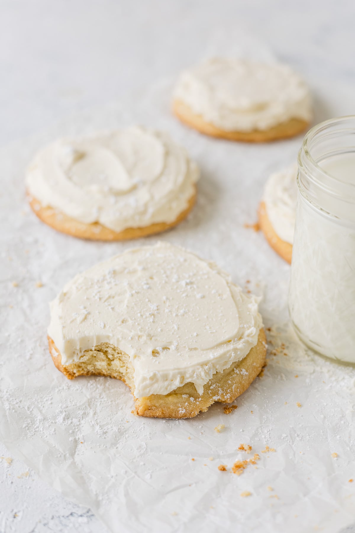 A vanilla frosted sugar cookie sprinkled with powdered sugar with a bite removed.