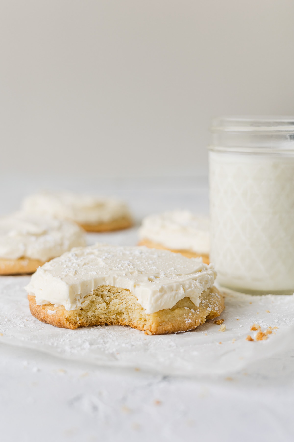 A vanilla frosted sugar cookie with a bite removed and a glass of milk.