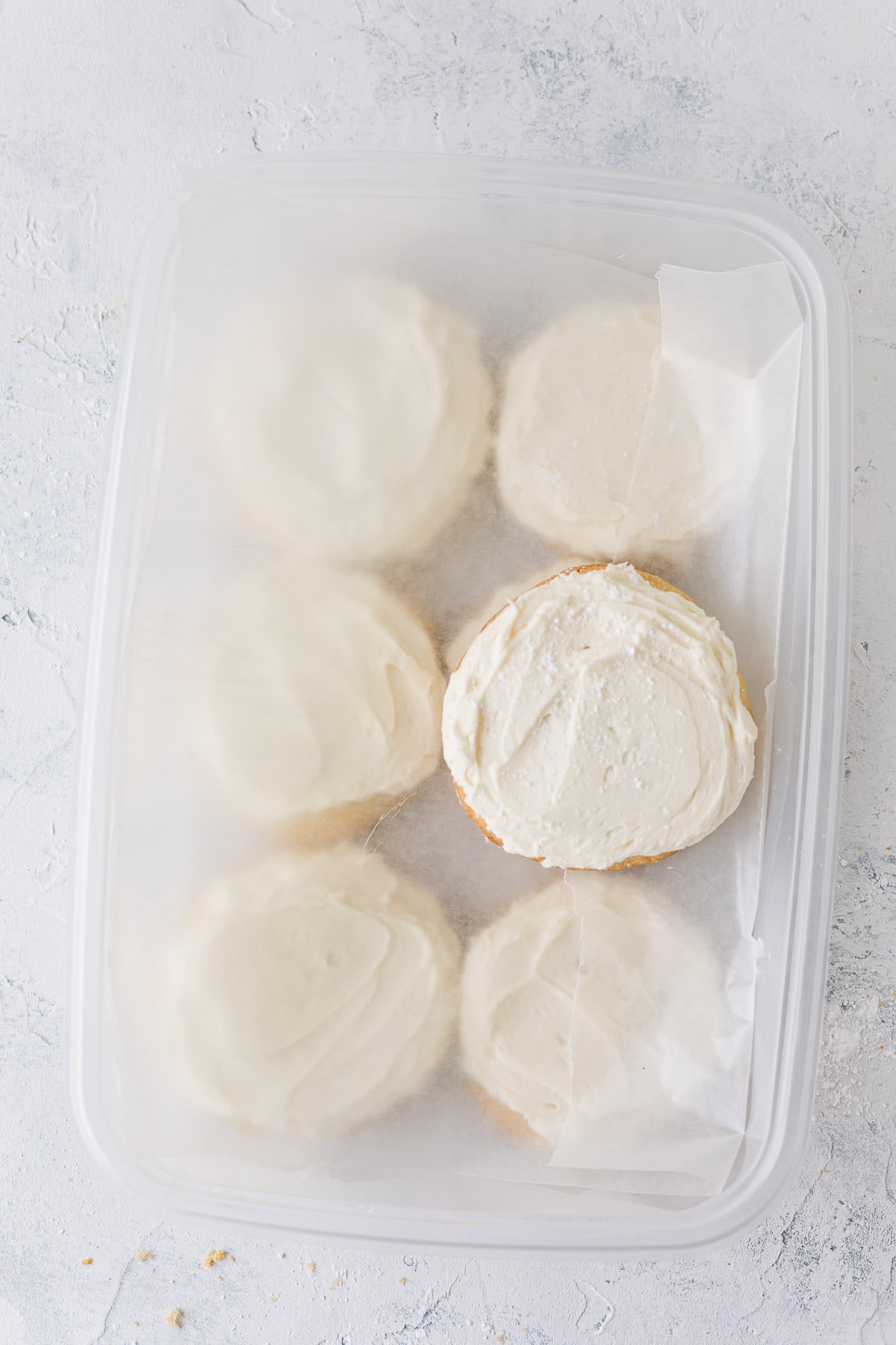 Frosted sugar cookies layered in a plastic storage box with lid removed.