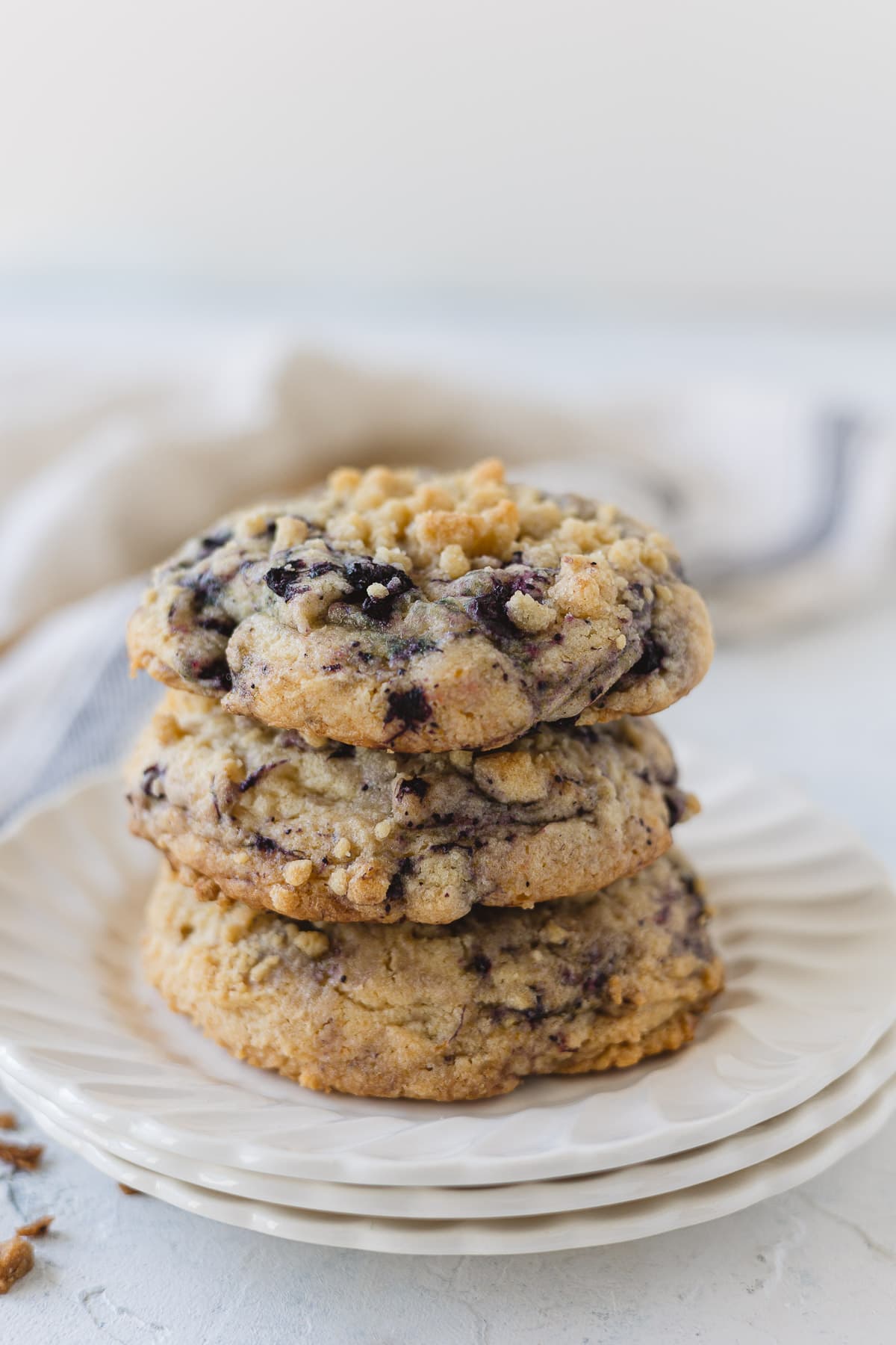 A stack of three blueberry muffin cookies on a stack of three white plates.