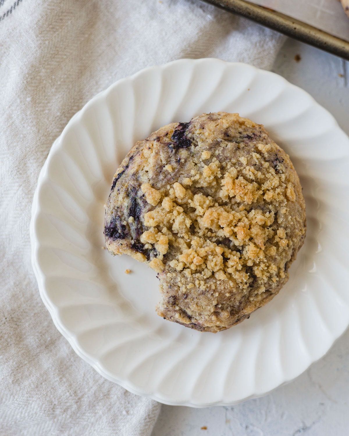 A Blueberry Muffin Cookie topped with streusel on a stack of white plates.