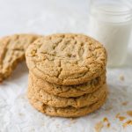 A stack of large Crumbl Classic Peanut Butter Cookies and a glass of milk.