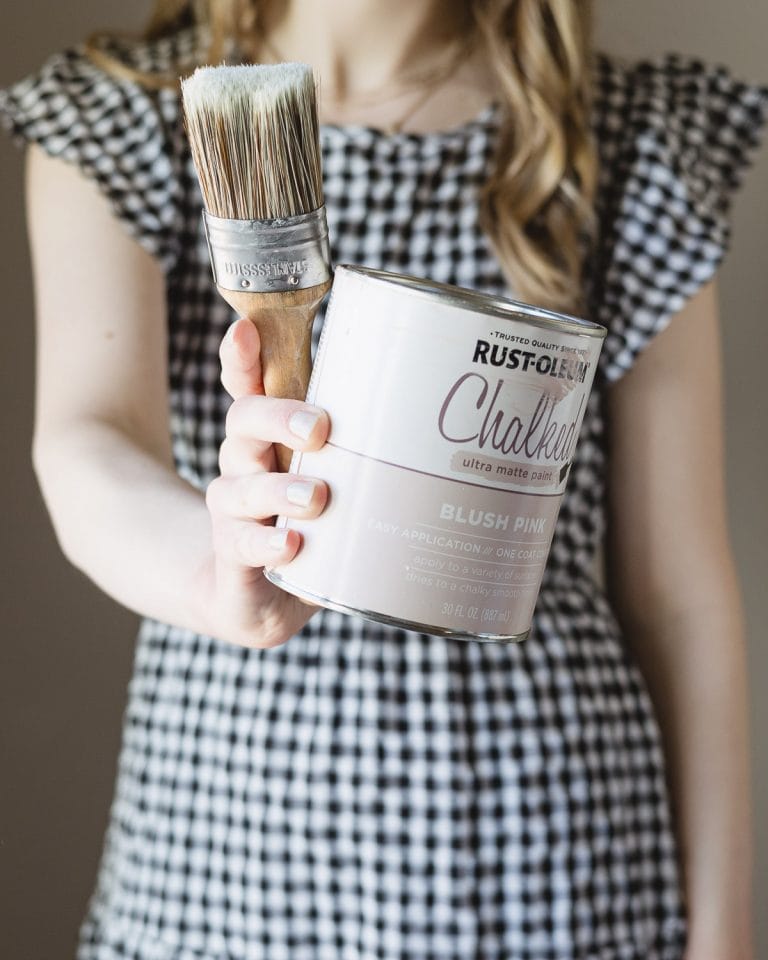 Woman holding a paint brush and can of pink chalk style paint.