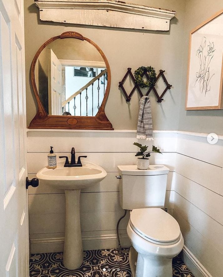 A farmhouse bathroom with half shiplap wall, antique mirror, and patterned tile floor.