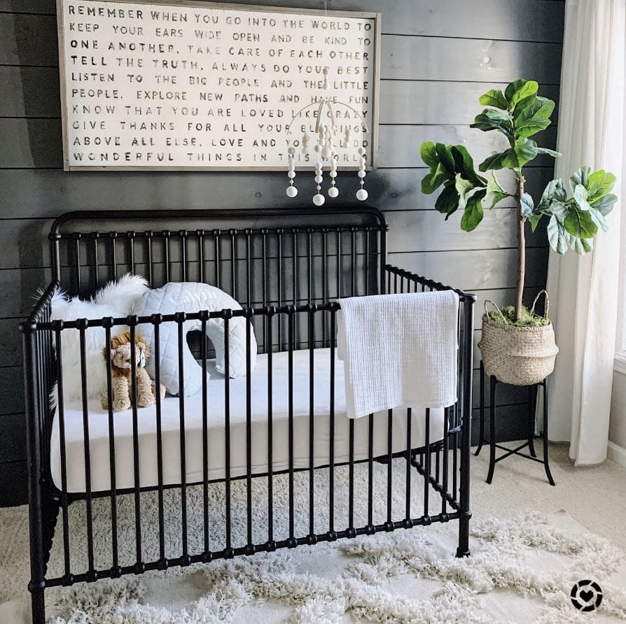 A baby nursery with a black shiplap accent wall, spindle crib, and fluffy rug.