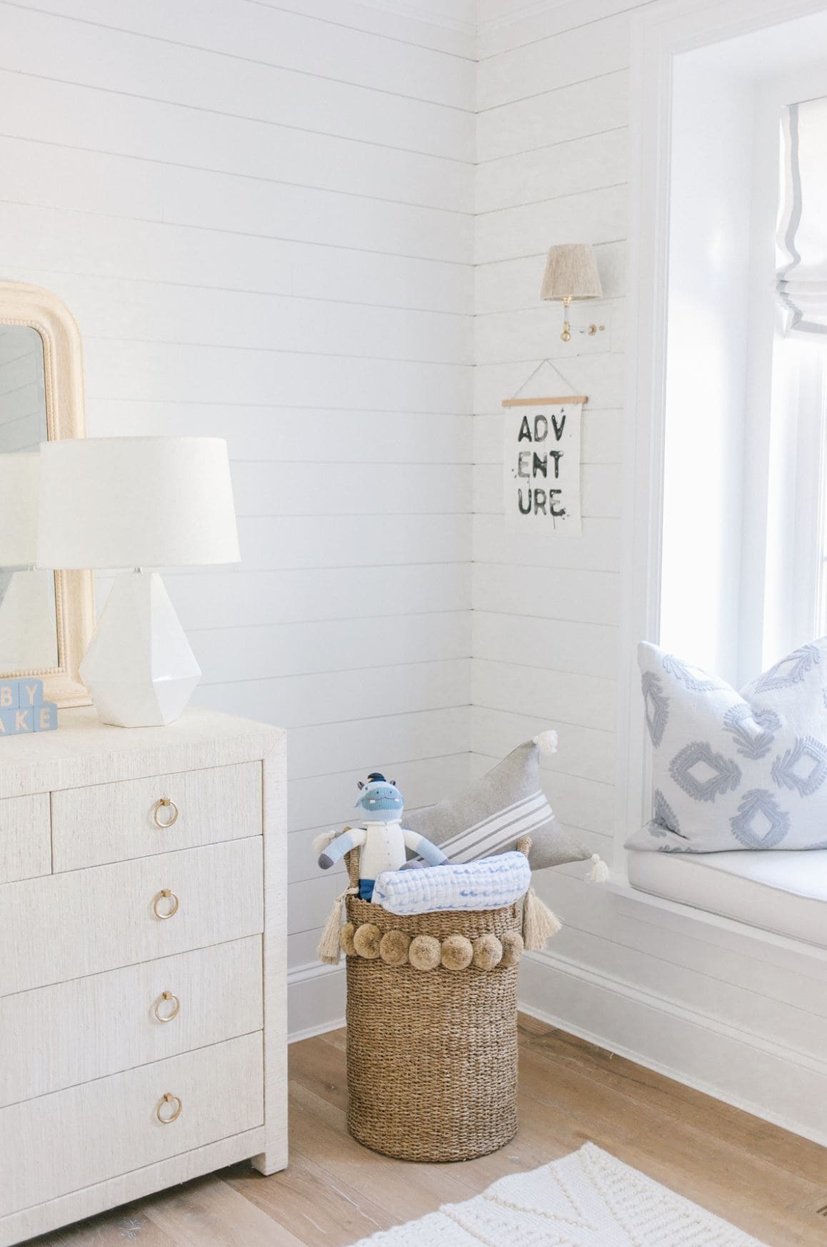 A cozy corner of a baby's nursery with shiplap walls, dresser, and bin of toys.