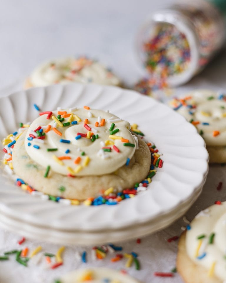 A frosted funfetti cookie on a stack of scalloped white plates.