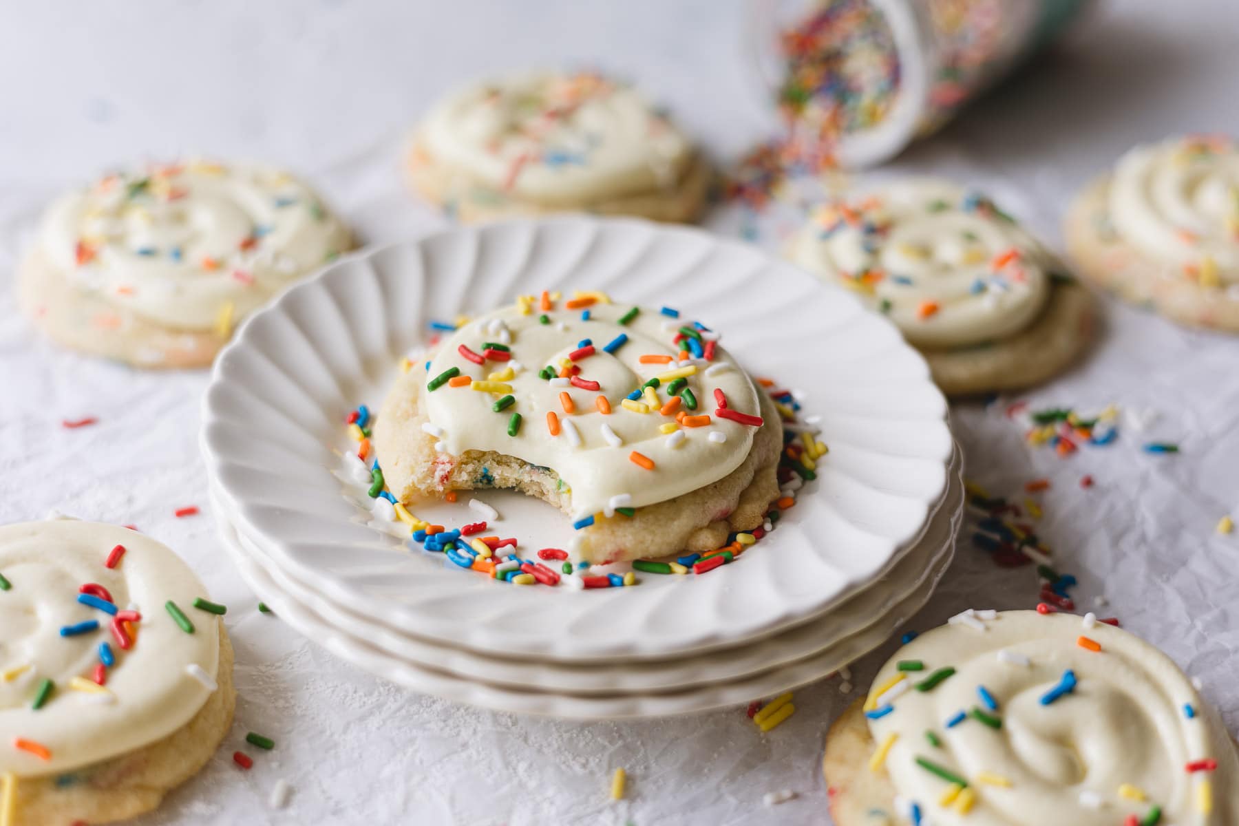A Crumbl Funfetti Copycat cookie with a bite removed on a stack of plates.