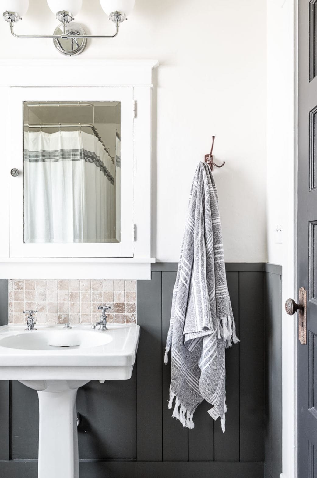 A small sink with a mirror above and dark gray vertical shiplap.