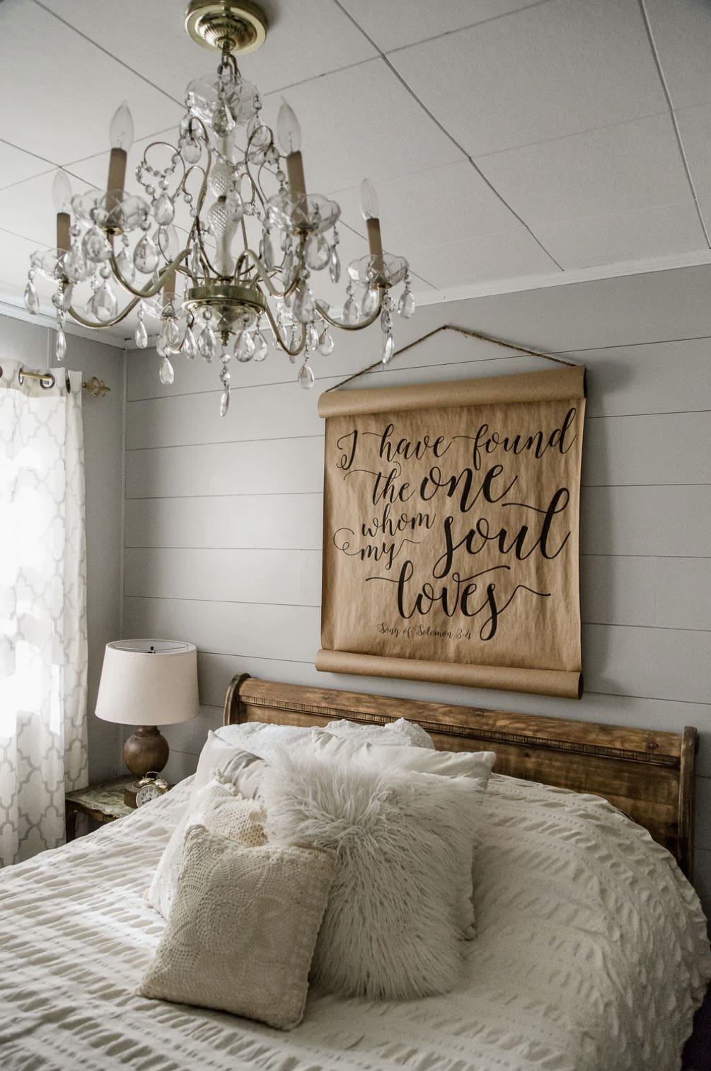 A bedroom with a gray shiplap accent wall over the bed and a hand-lettered sign.