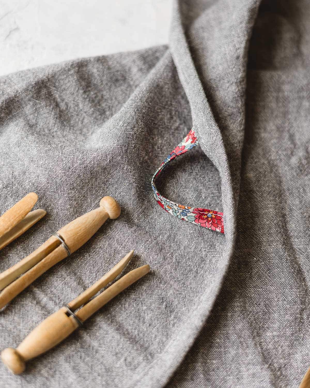 Close up view of a floral bias tape loop on a blue-gray linen kitchen towel and vintage clothespins.