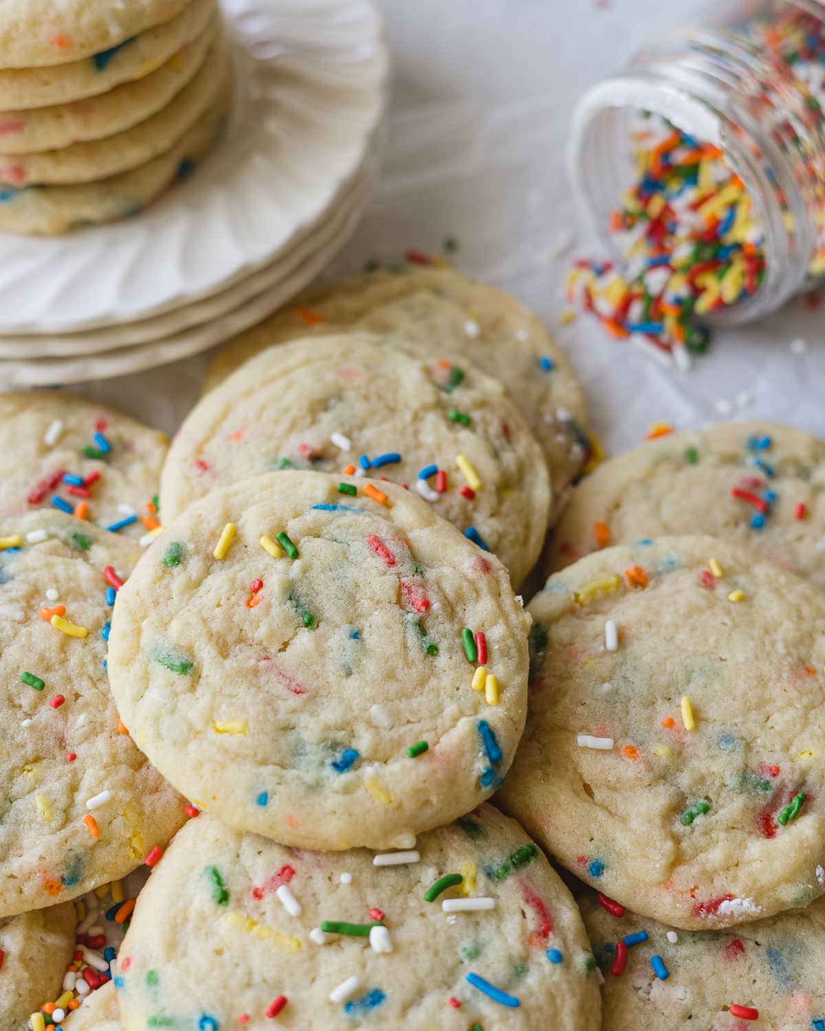 Funfetti sugar cookies piled up with a jar of sprinkles near by.