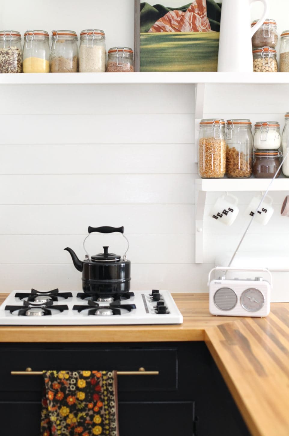 A kitchen with a shiplap backsplash, wood countertops, and black cupboards.