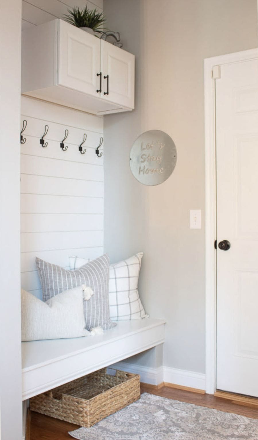 A shiplap mudroom area with storage hooks and a bench with pillows.