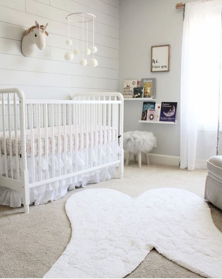 A baby nursery with a white spindle crib, shiplap wall, and small bookshelves.