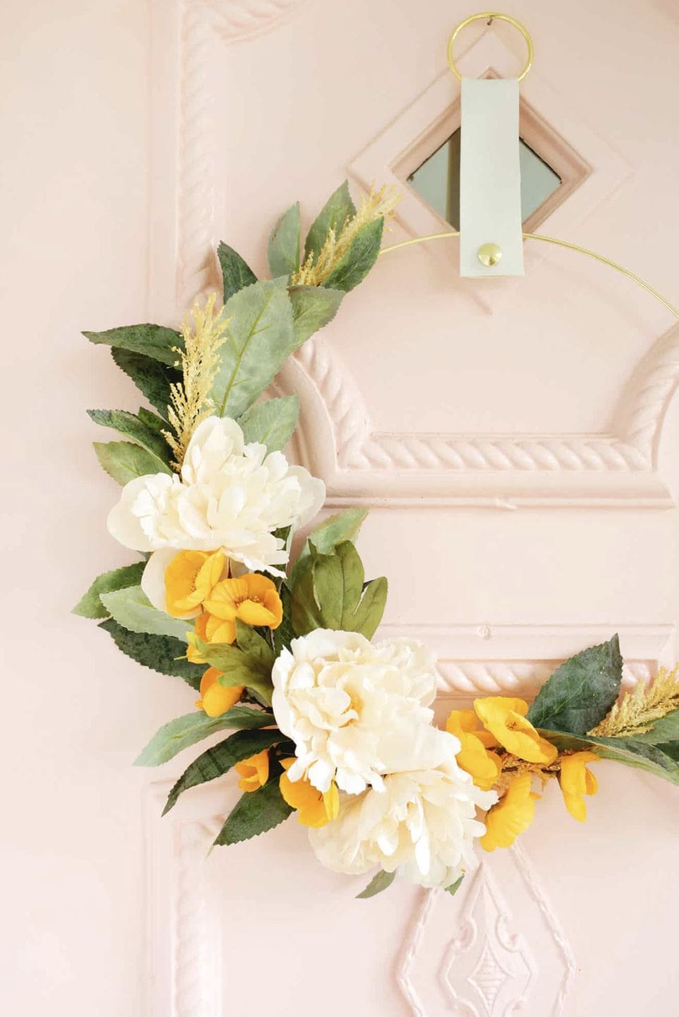 A white and yellow floral wreath hanging on a pink door.