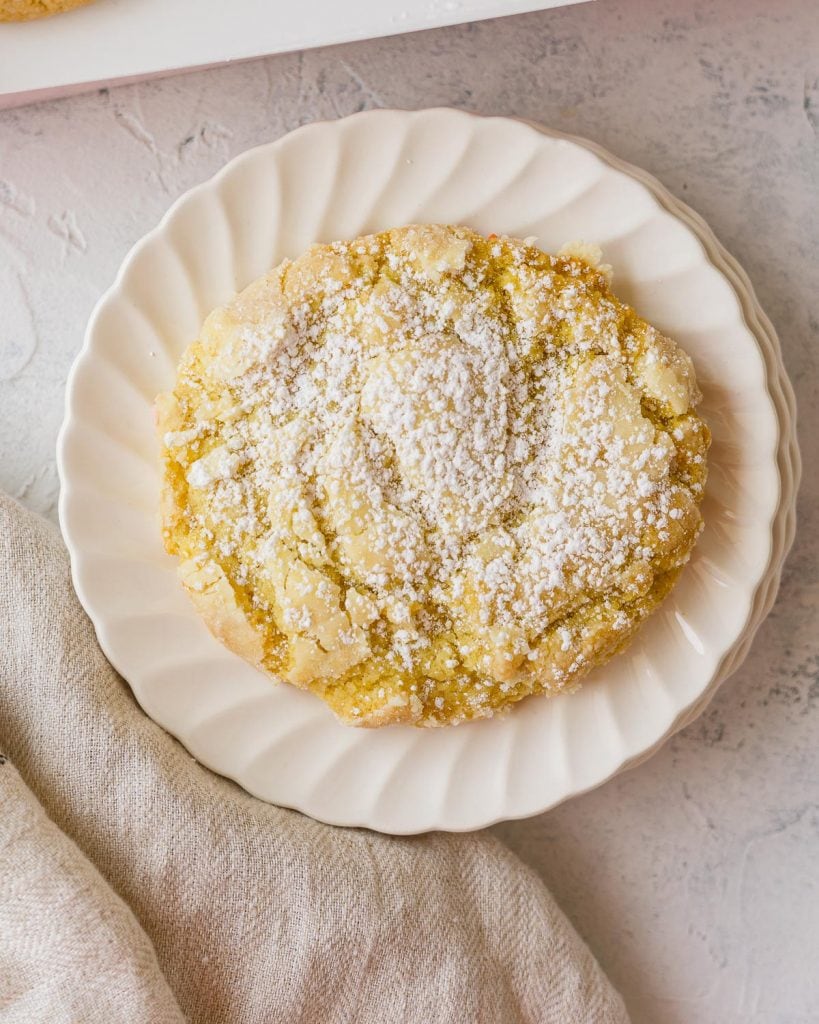 A lemon crinkle Crumbl Cookie topped with powdered sugar on a scalloped plate.