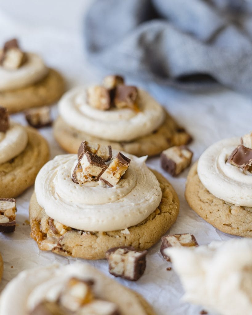 Snicker Peanut Butter Cookies frosted with swirls of caramel frosting and chunks of chopped Snickers bars.