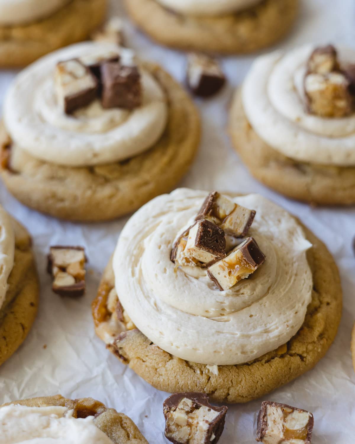 A peanut butter cookie topped with caramel buttercream and chopped Snickers pieces.