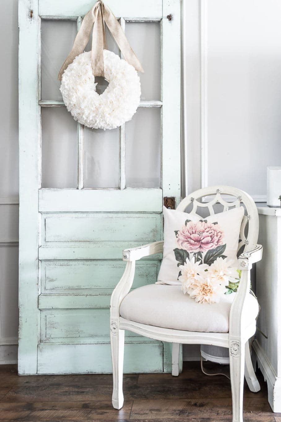 A white DIY coffee filter wreath hanging on a vintage door alongside a vintage chair.