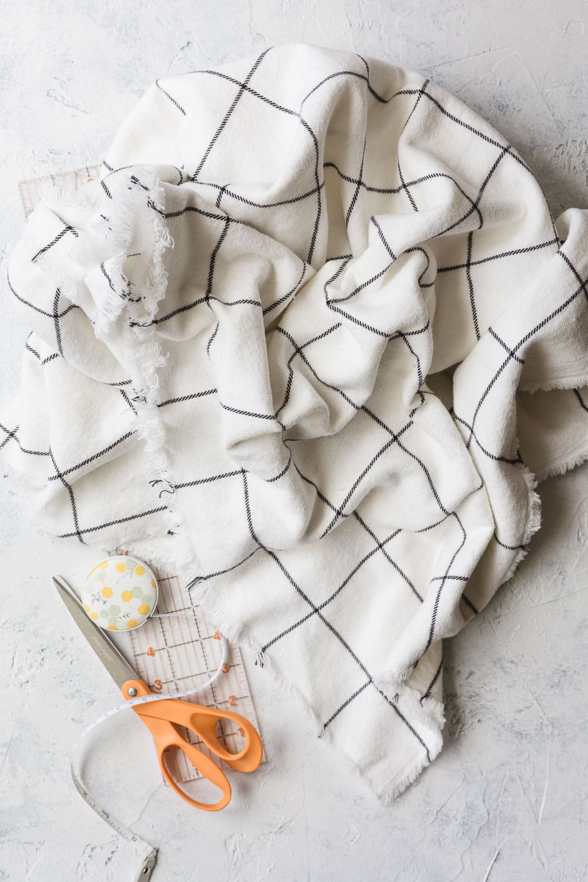 A large piece of white fabric with black grid design, a ruler, scissors, and tape measure.