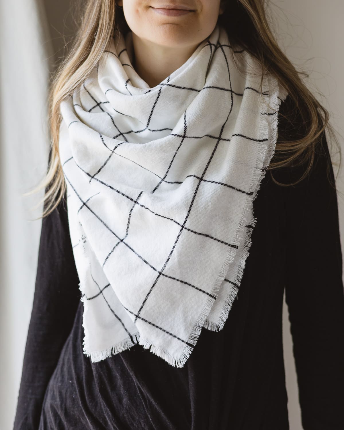 Woman wearing a black shirt and white blanket scarf with a black grid design.