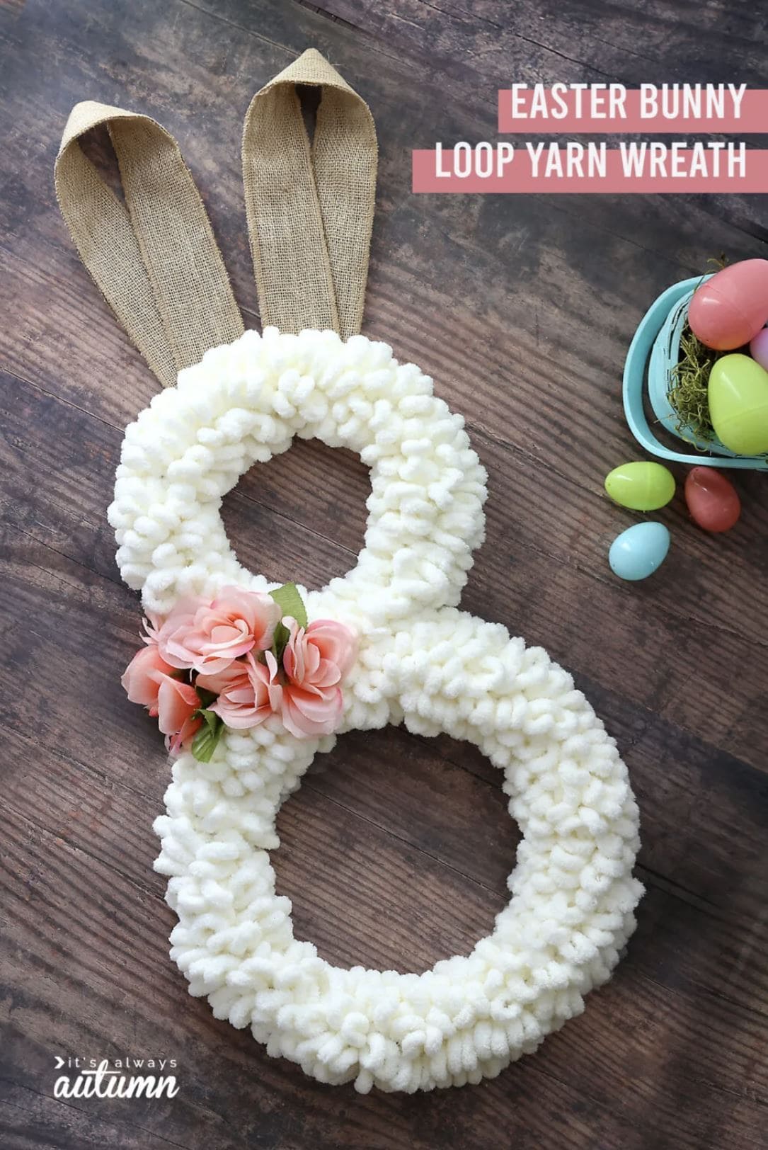 A DIY bunny wreath with two yarn-covered hoops, burlap ears, and floral decoration.