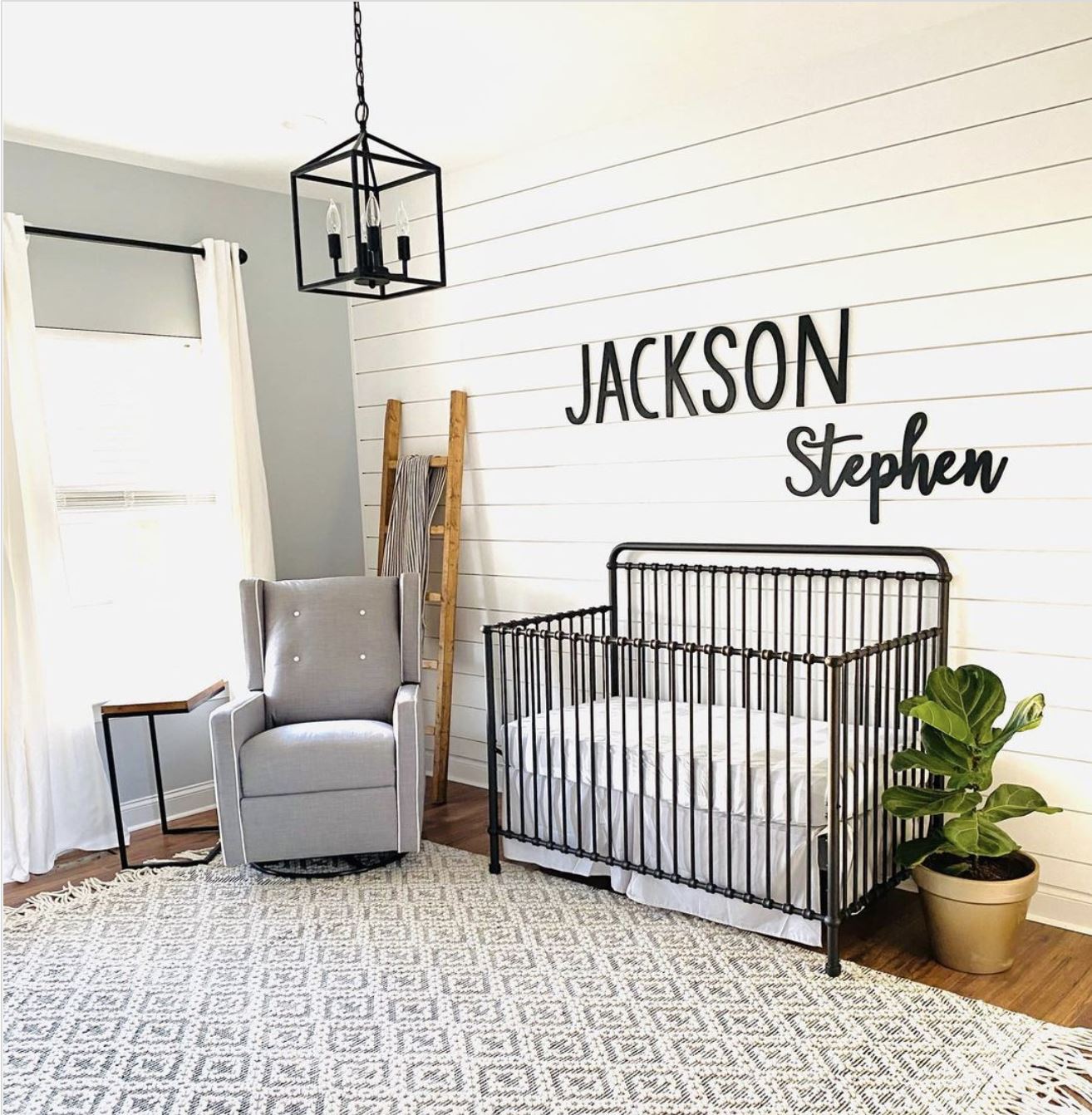 A farmhouse nursery with a shiplap feature wall, large rug, and black crib.