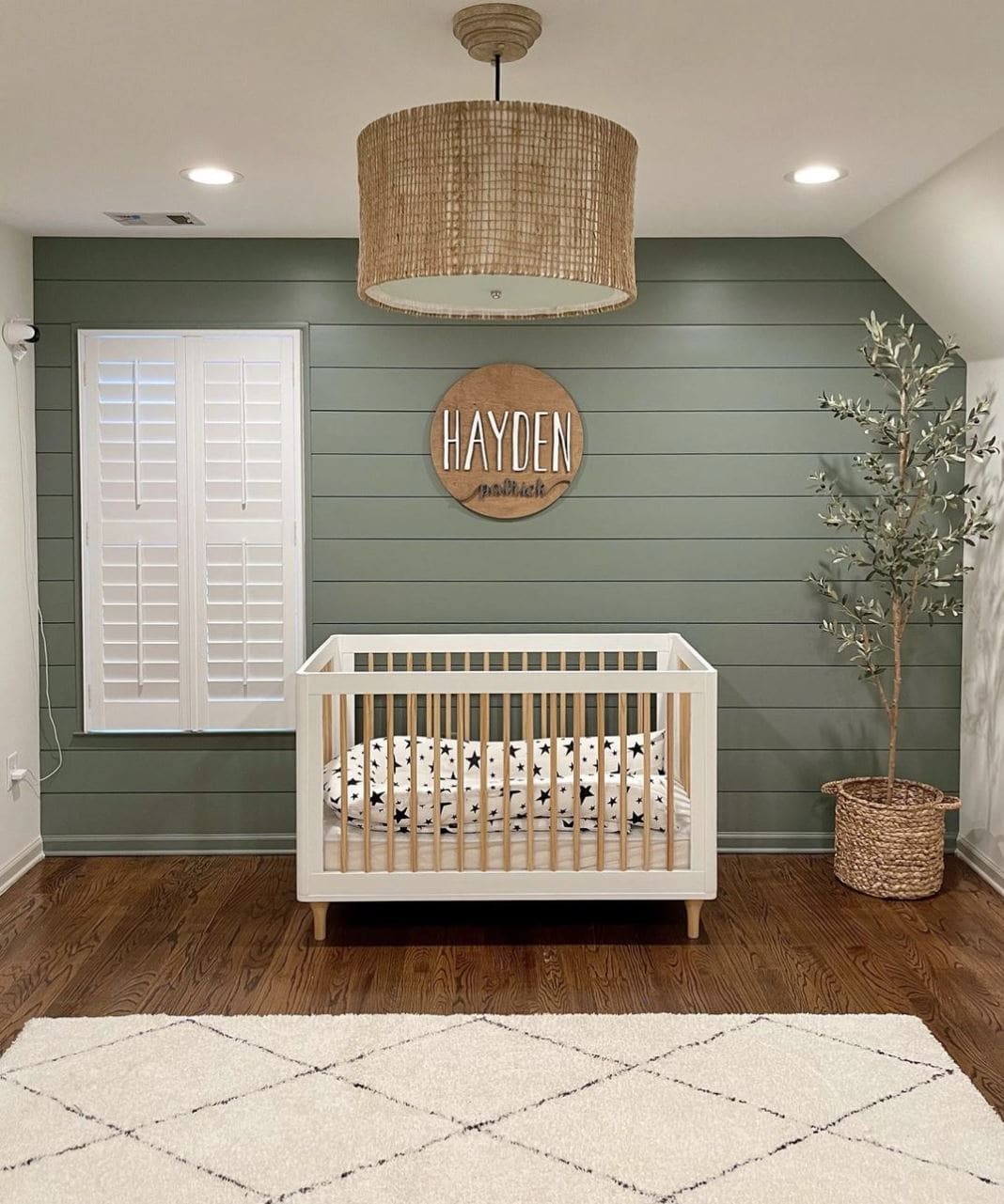 A modern baby nursery with green shiplap feature wall.