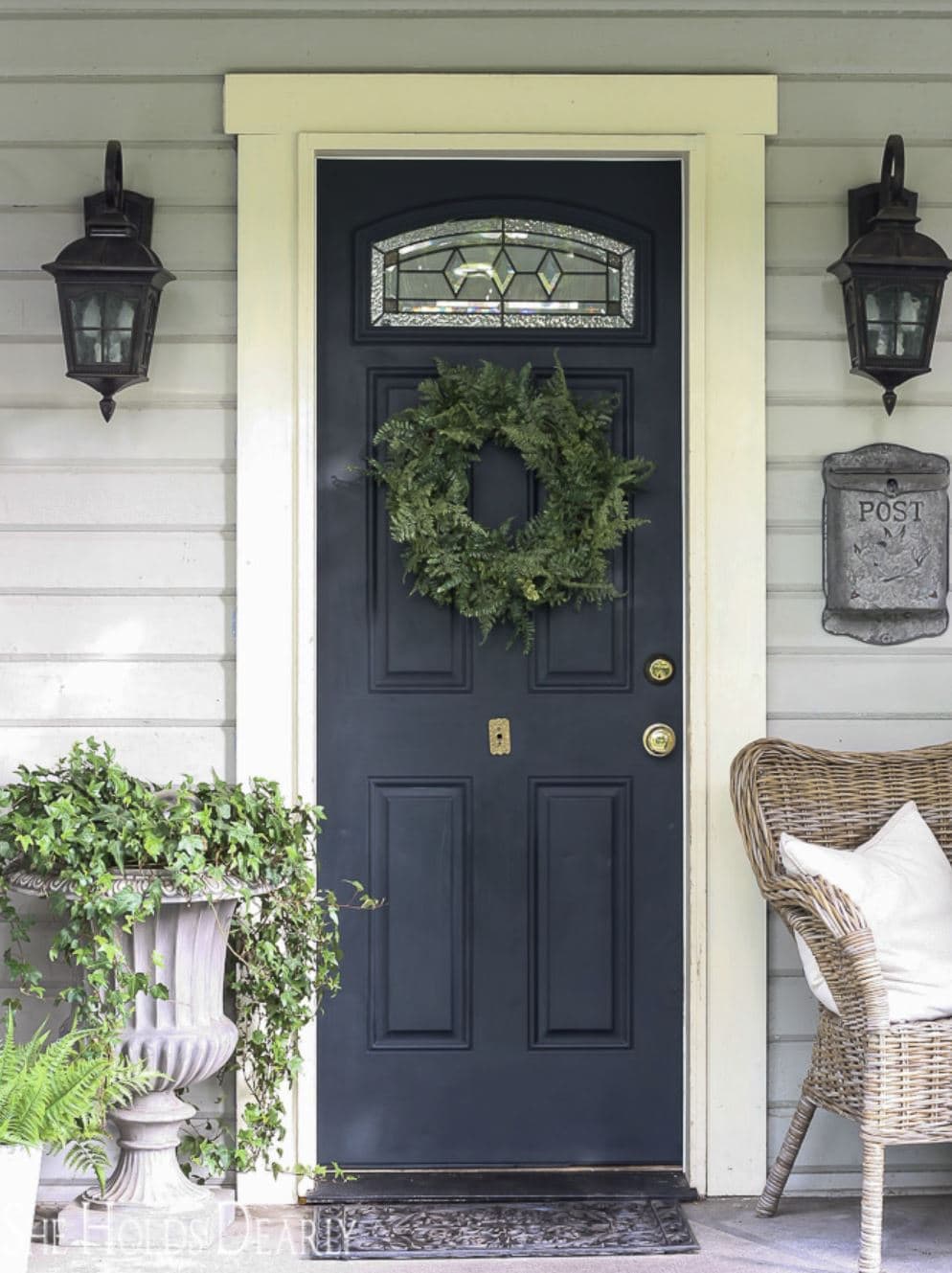 A black front door with a fern wreath hanging on it.